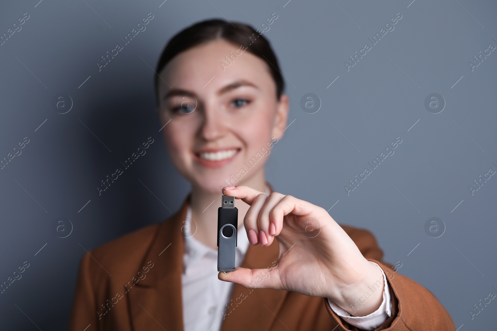 Photo of Woman holding usb flash drive on grey background, closeup