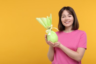 Photo of Easter celebration. Happy woman with wrapped egg on orange background, space for text