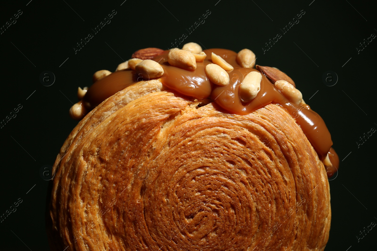 Photo of Round croissant with chocolate paste and nuts on black background, closeup. Tasty puff pastry
