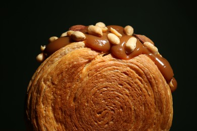Photo of Round croissant with chocolate paste and nuts on black background, closeup. Tasty puff pastry