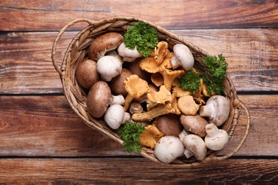 Photo of Basket with different mushrooms on wooden table, top view