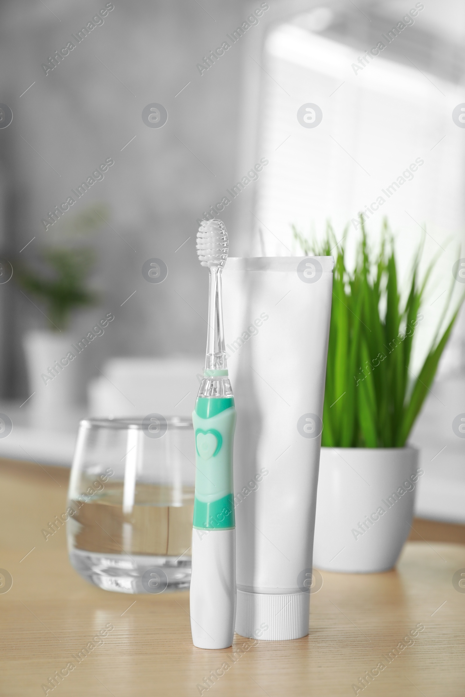 Photo of Electric toothbrush, tube with paste and glass of water on wooden table in bathroom