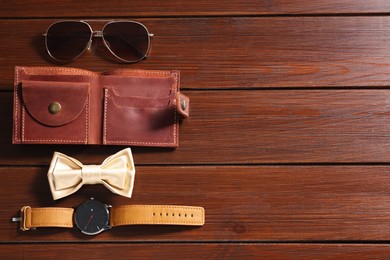 Photo of Stylish pale yellow bow tie, brown wallet, wristwatch and sunglasses on wooden table, flat lay. Space for text
