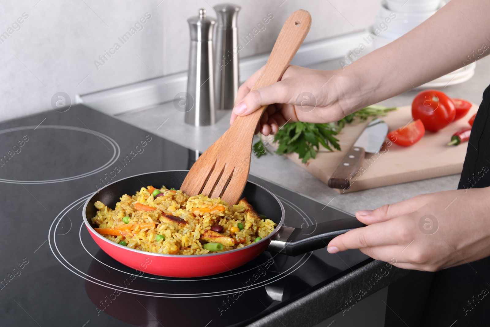 Photo of Woman frying rice with meat and vegetables on induction stove in kitchen, closeup