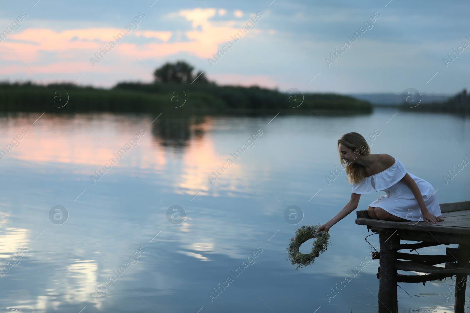 Photo of Young woman putting wreath made of beautiful flowers in water