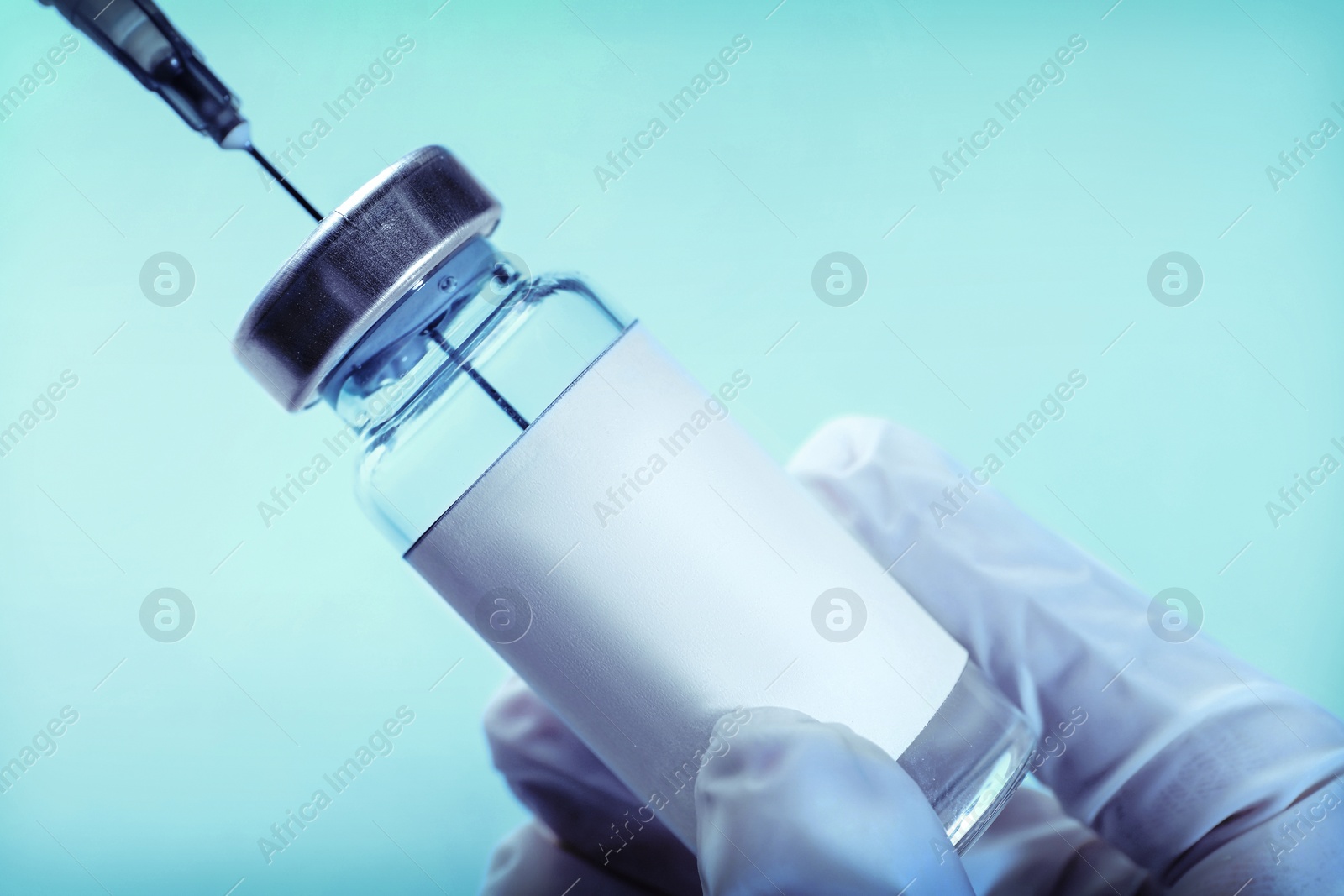 Image of Laboratory worker filling syringe with medication from vial on light blue background, closeup