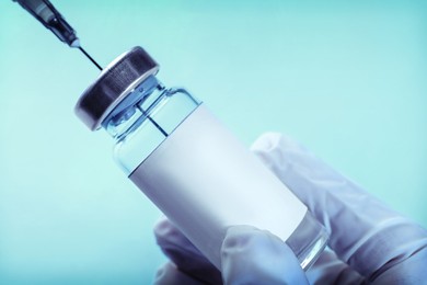Laboratory worker filling syringe with medication from vial on light blue background, closeup
