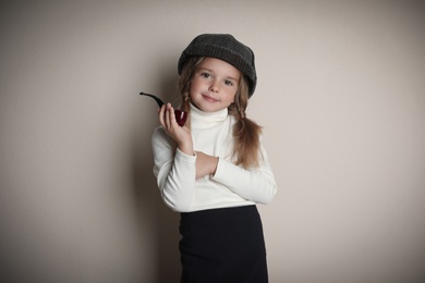 Photo of Cute little child in hat with smoking pipe playing detective on beige background