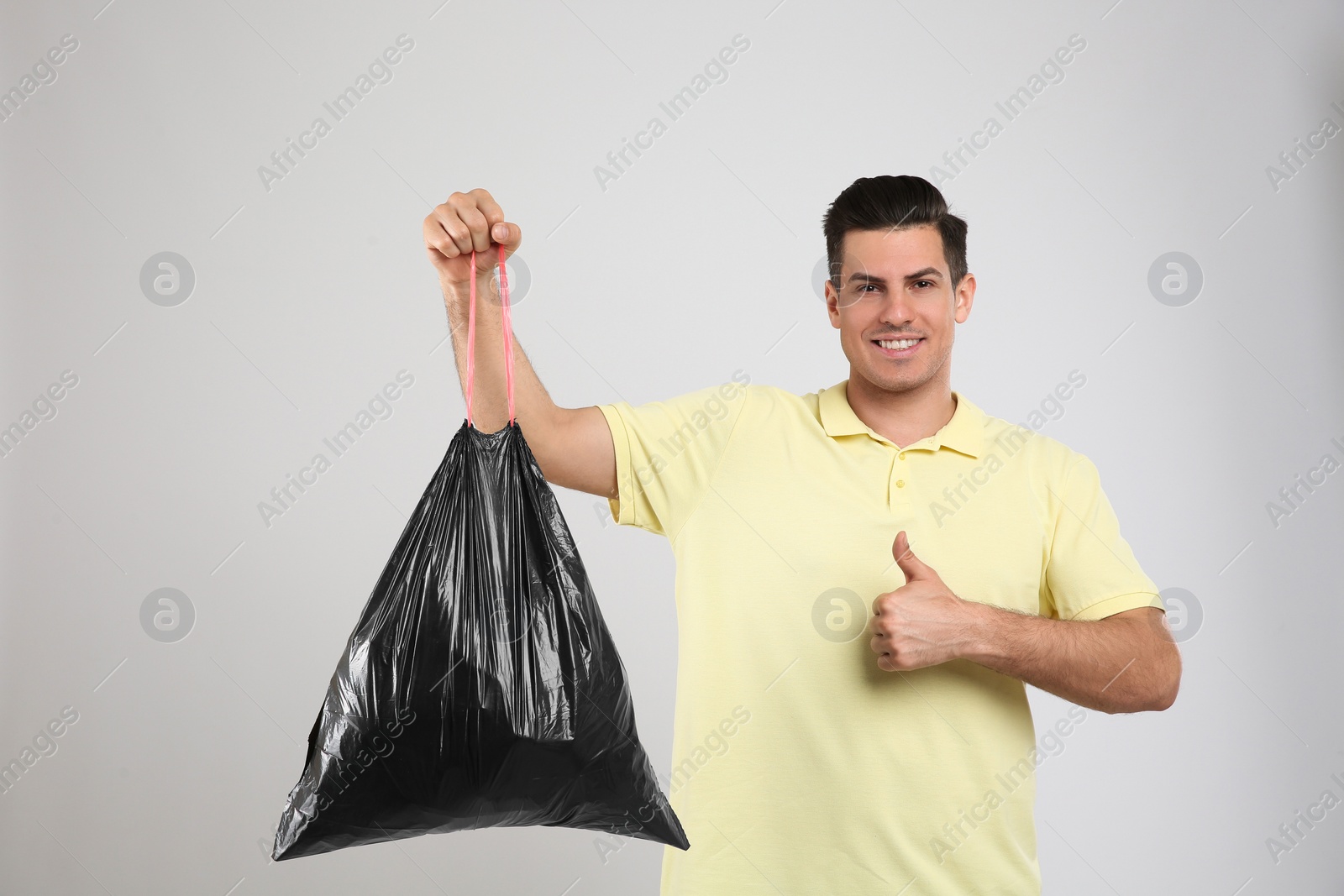 Photo of Man holding full garbage bag on light background