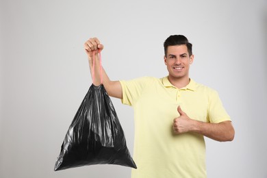 Man holding full garbage bag on light background