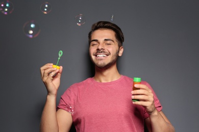 Young man blowing soap bubbles on color background