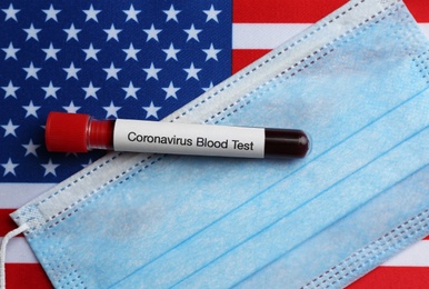 Photo of Test tube with blood sample and medical mask on American flag, flat lay. Coronavirus pandemic in USA