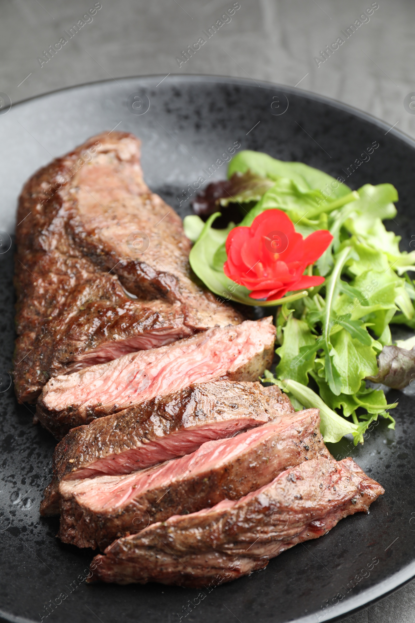 Photo of Pieces of delicious grilled beef meat and greens on table, closeup