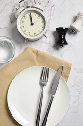 Photo of Flat lay composition with plate, cutlery and alarm clock on white marble table. Business lunch concept