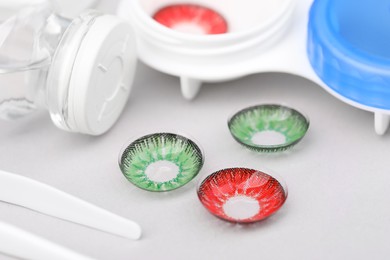 Photo of Different color contact lenses and tweezers on white background, closeup