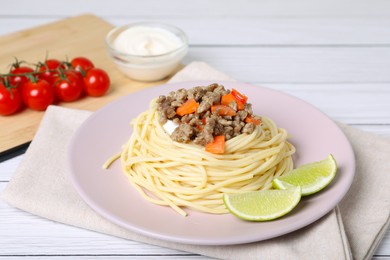 Tasty minced meat with spaghetti, vegetables and lime on white wooden table, closeup
