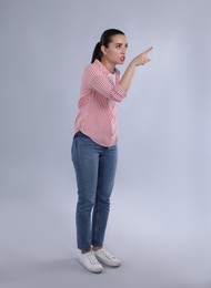 Photo of Emotional woman pointing with index finger on light grey background