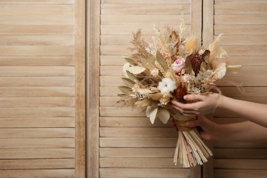 Woman holding beautiful dried flower bouquet on wooden background, closeup. Space for text