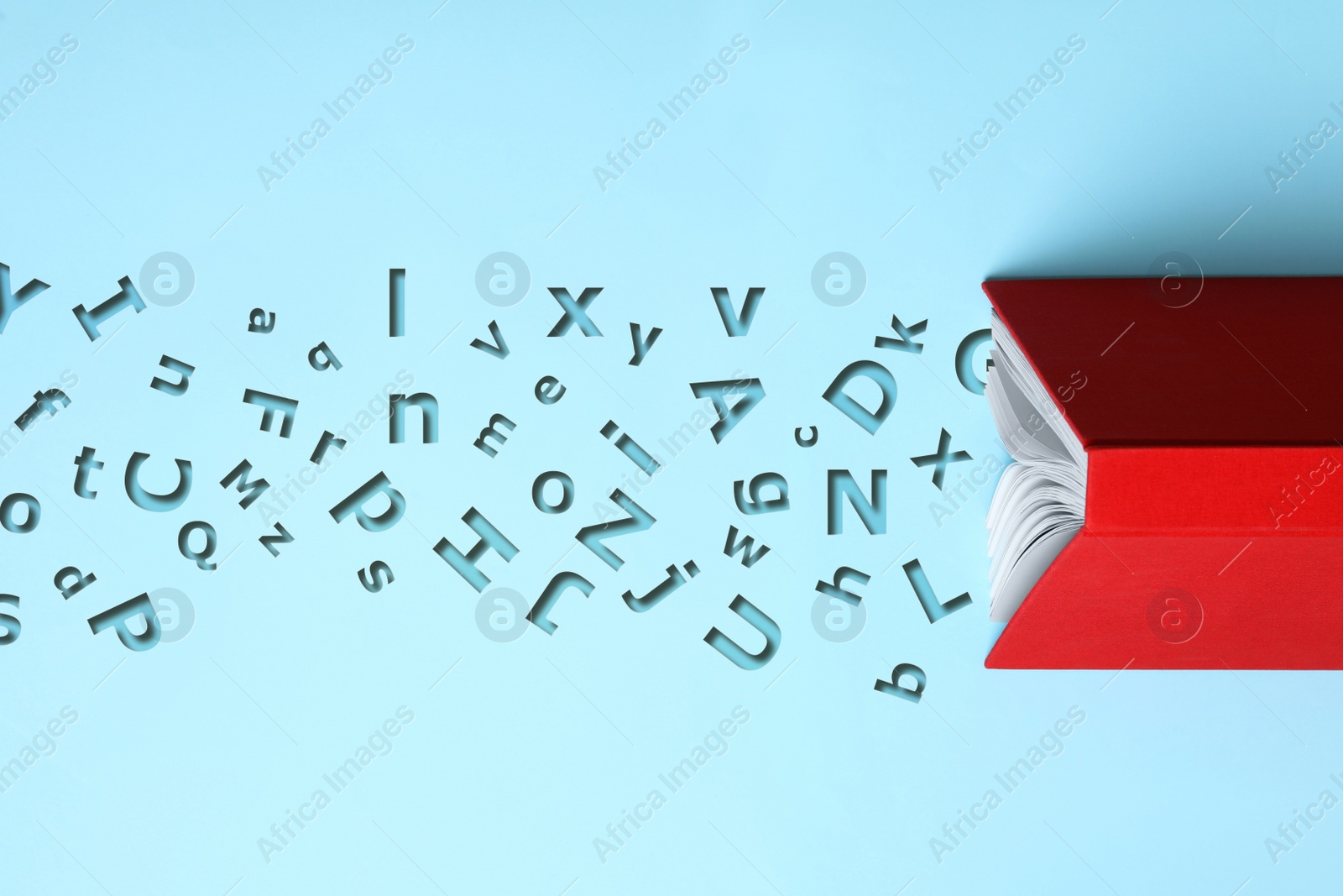 Image of Open book with letters on light blue background, top view. Dyslexia concept