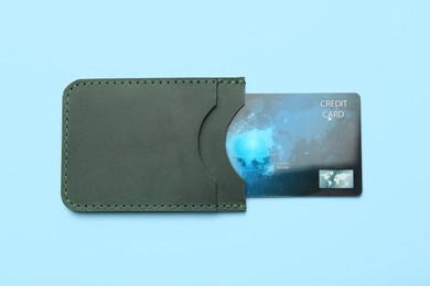 Leather card holder with credit card on light blue background, top view