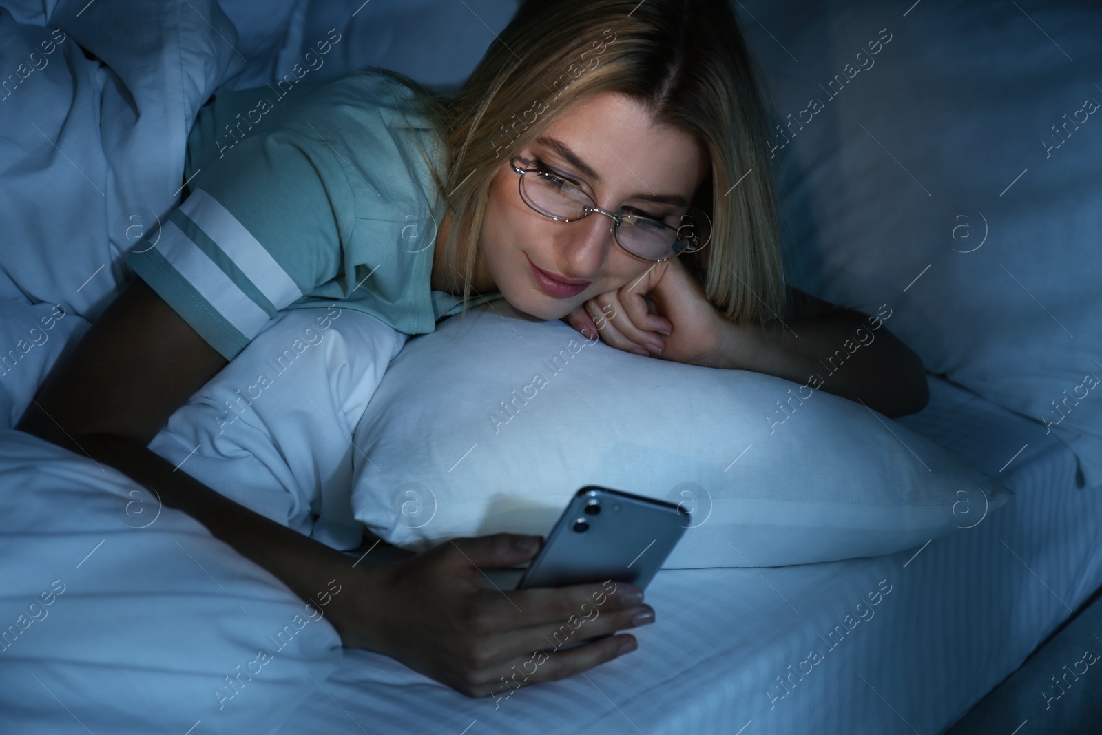 Photo of Young woman using smartphone in bed at night. Nomophobia and sleeping disorder problem