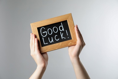 Woman holding blackboard with words GOOD LUCK on light grey background, closeup