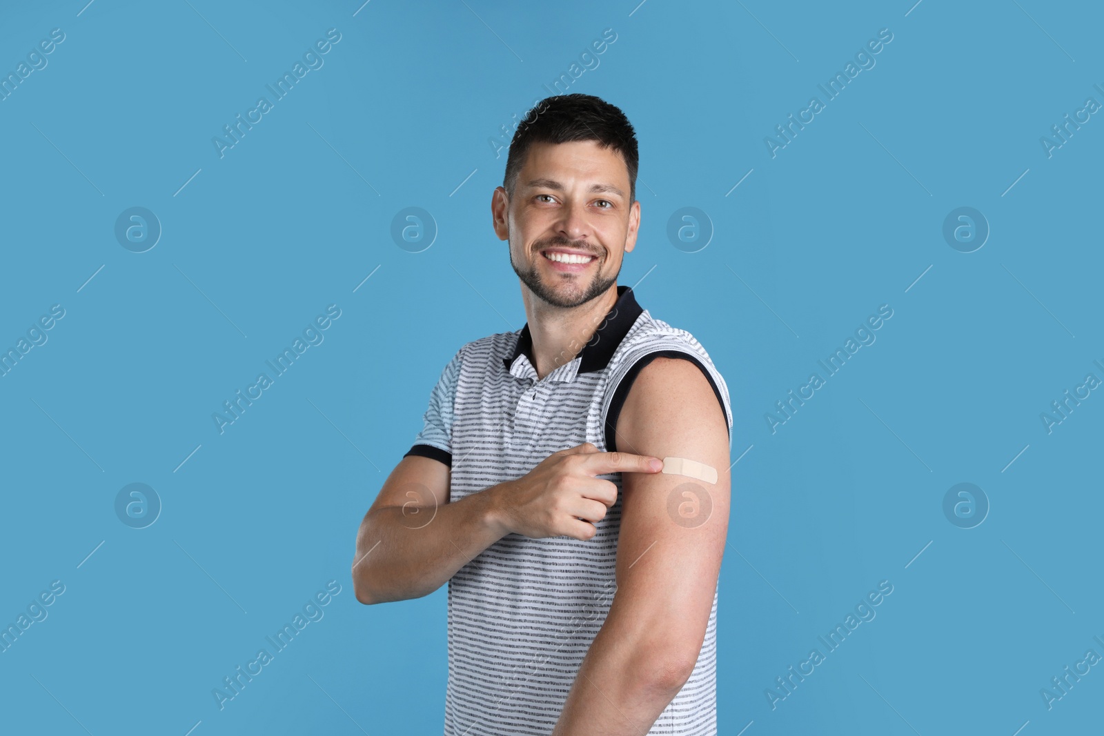 Photo of Vaccinated man showing medical plaster on his arm against light blue background