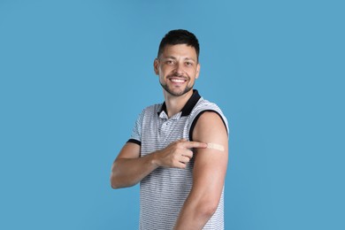 Photo of Vaccinated man showing medical plaster on his arm against light blue background