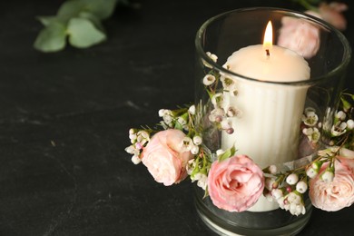 Photo of Glass holder with burning candle and floral decor on black stone table, closeup. Space for text