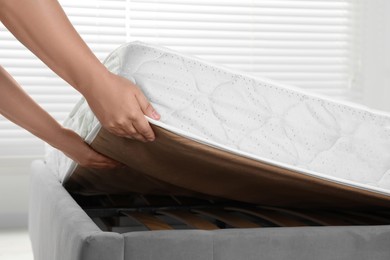 Photo of Woman putting soft light green mattress on gray bed indoors, closeup