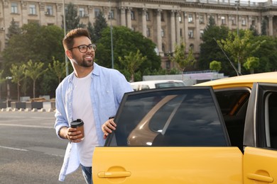 Photo of Handsome young man with coffee getting out of taxi on city street