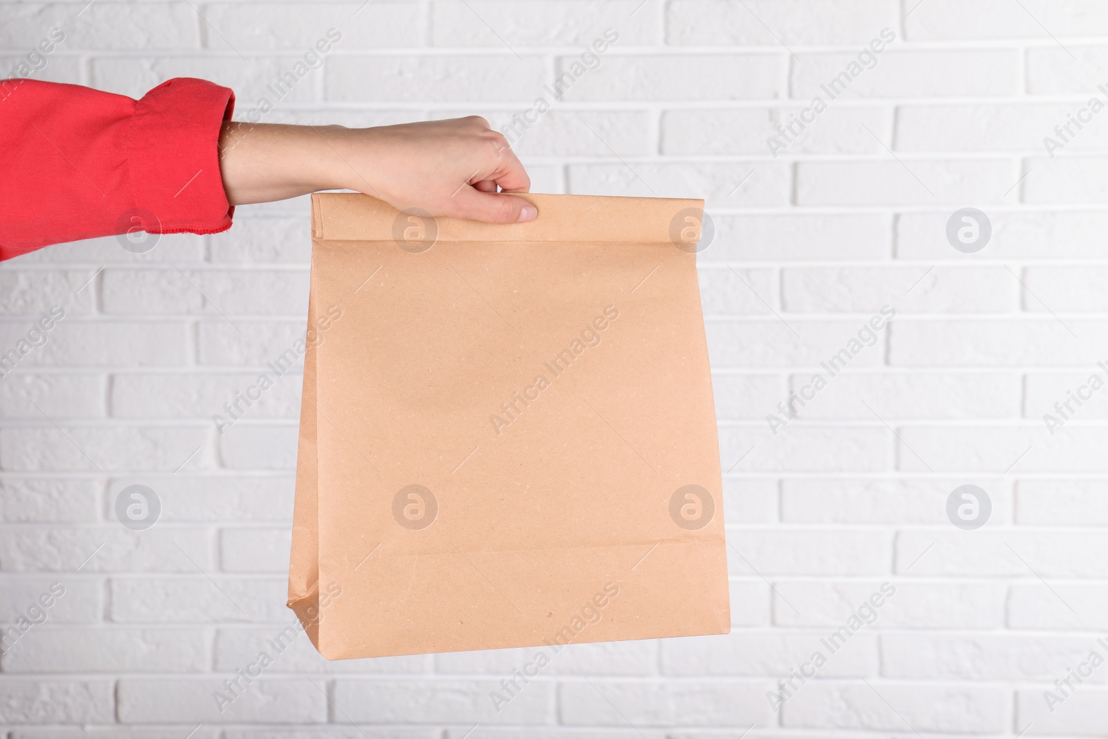 Photo of Woman holding paper bag against brick wall. Mockup for design