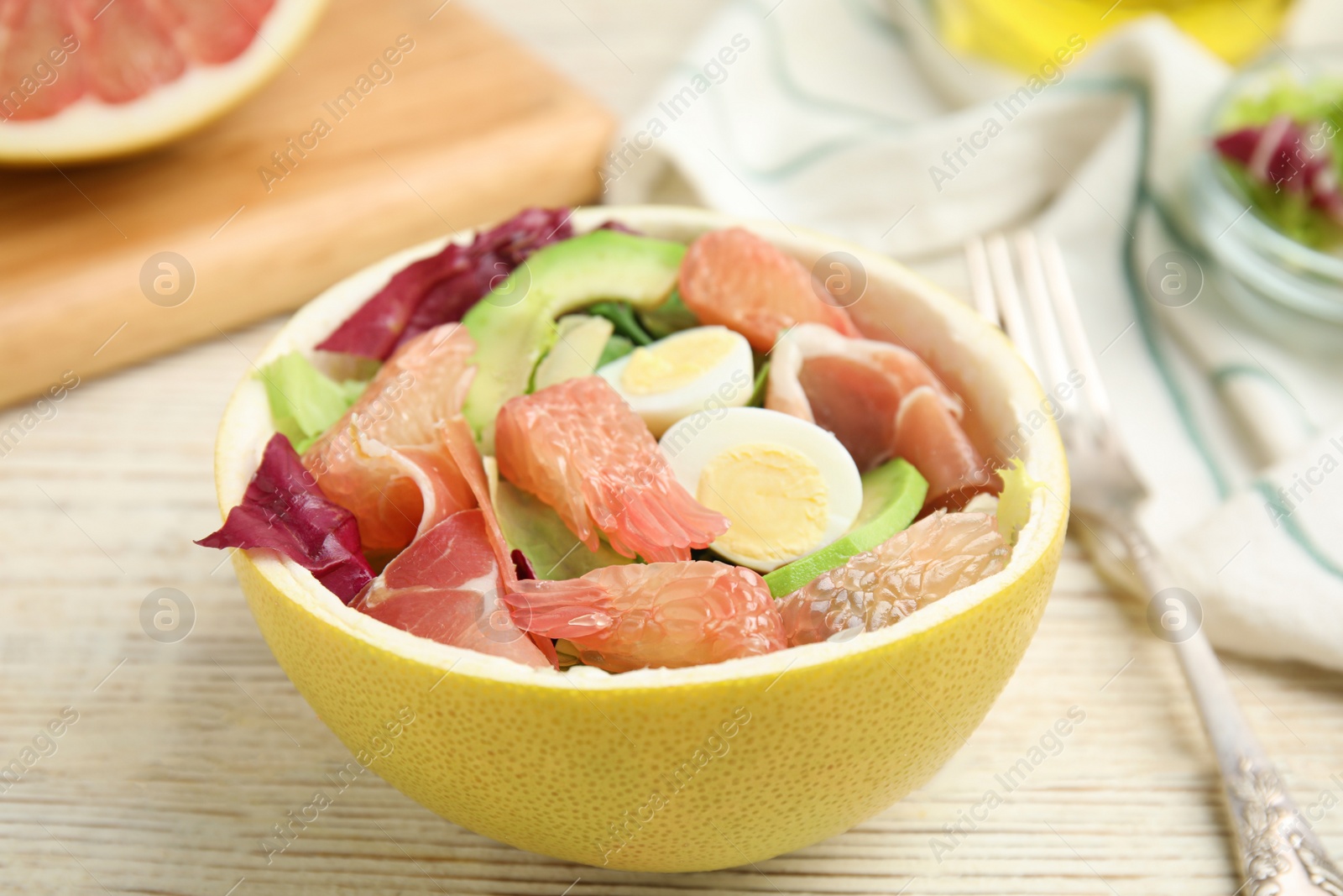 Photo of Delicious pomelo salad with prosciutto in half of fruit on white wooden table, closeup