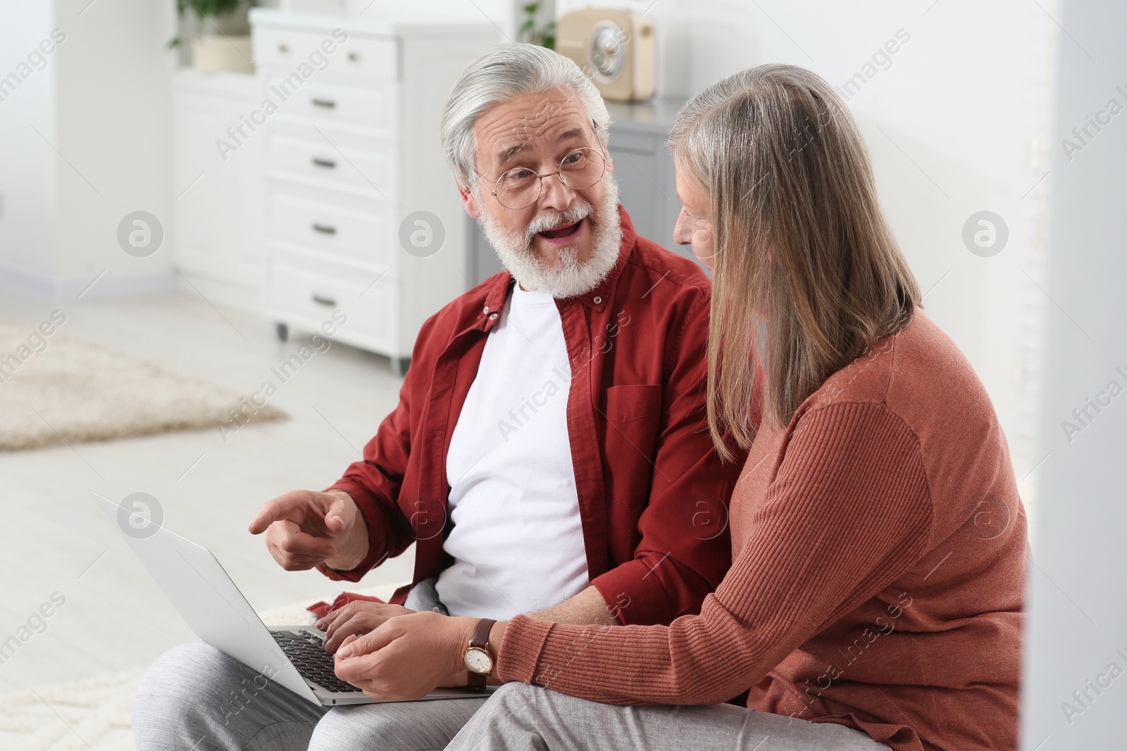 Photo of Senior couple using laptop on sofa at home