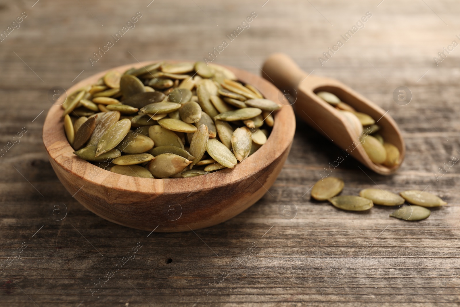 Photo of Bowl and scoop with peeled pumpkin seeds on wooden table