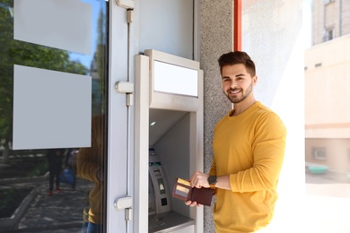 Young man with credit card near modern cash machine outdoors