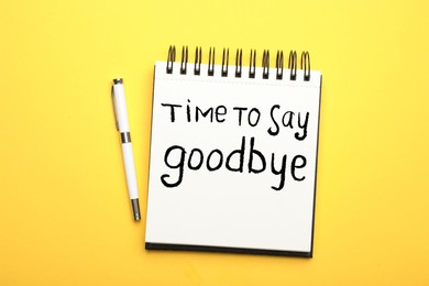 Image of Notebook with phrase Time to say Goodbye and pen on yellow background, top view