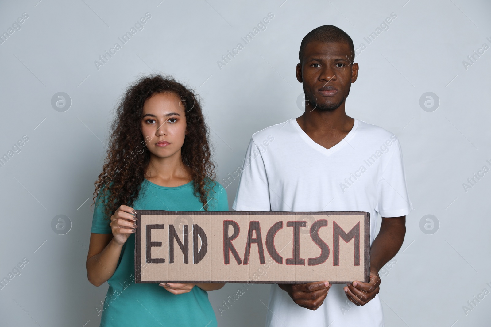 Photo of African American woman and man holding sign with phrase End Racism on grey background