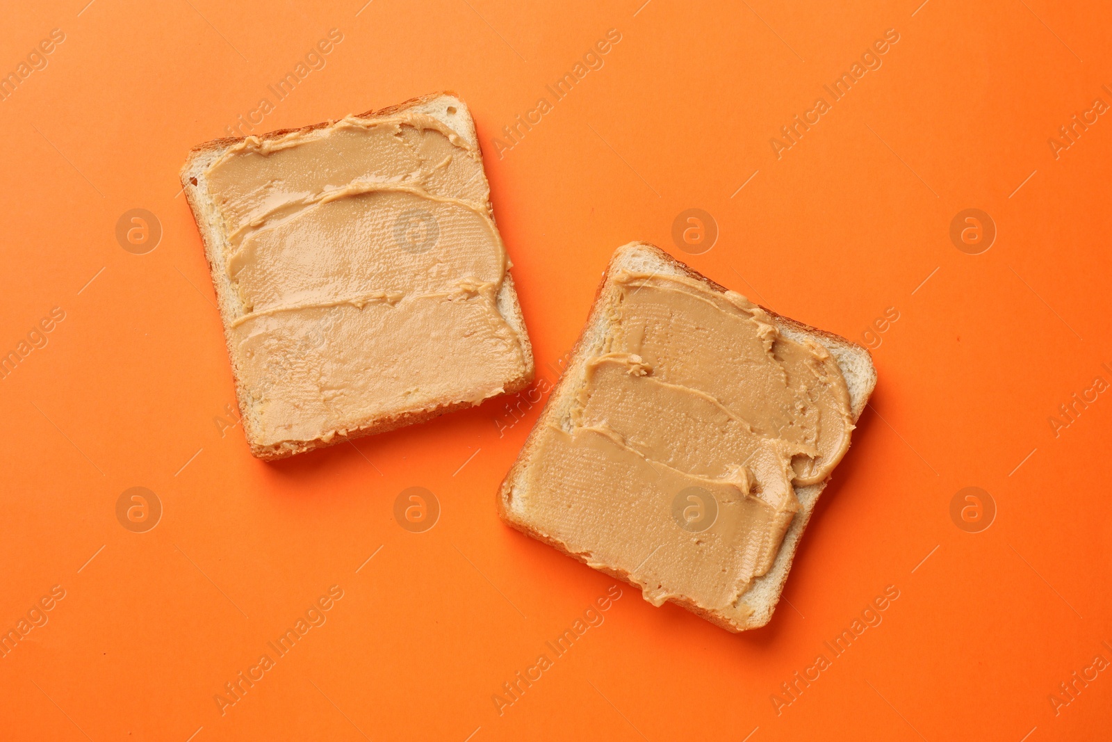 Photo of Tasty peanut butter sandwiches on orange background, flat lay