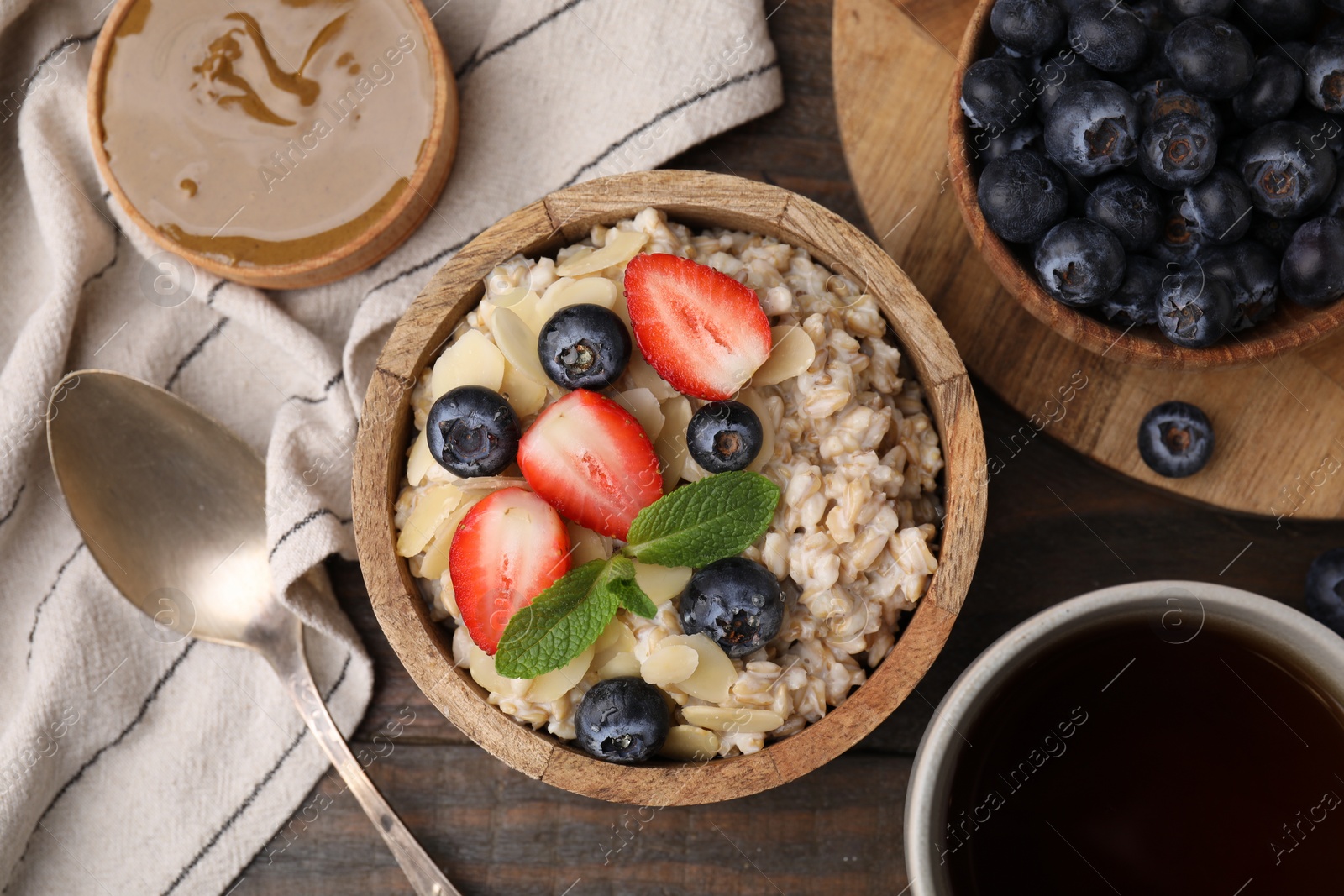 Photo of Tasty oatmeal with strawberries, blueberries and almond petals served on wooden table, flat lay