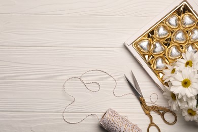 Photo of Delicious heart shaped chocolate candies, scissors and twine on white wooden table, flat lay. Space for text