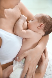 Young woman breastfeeding her baby on light background, closeup