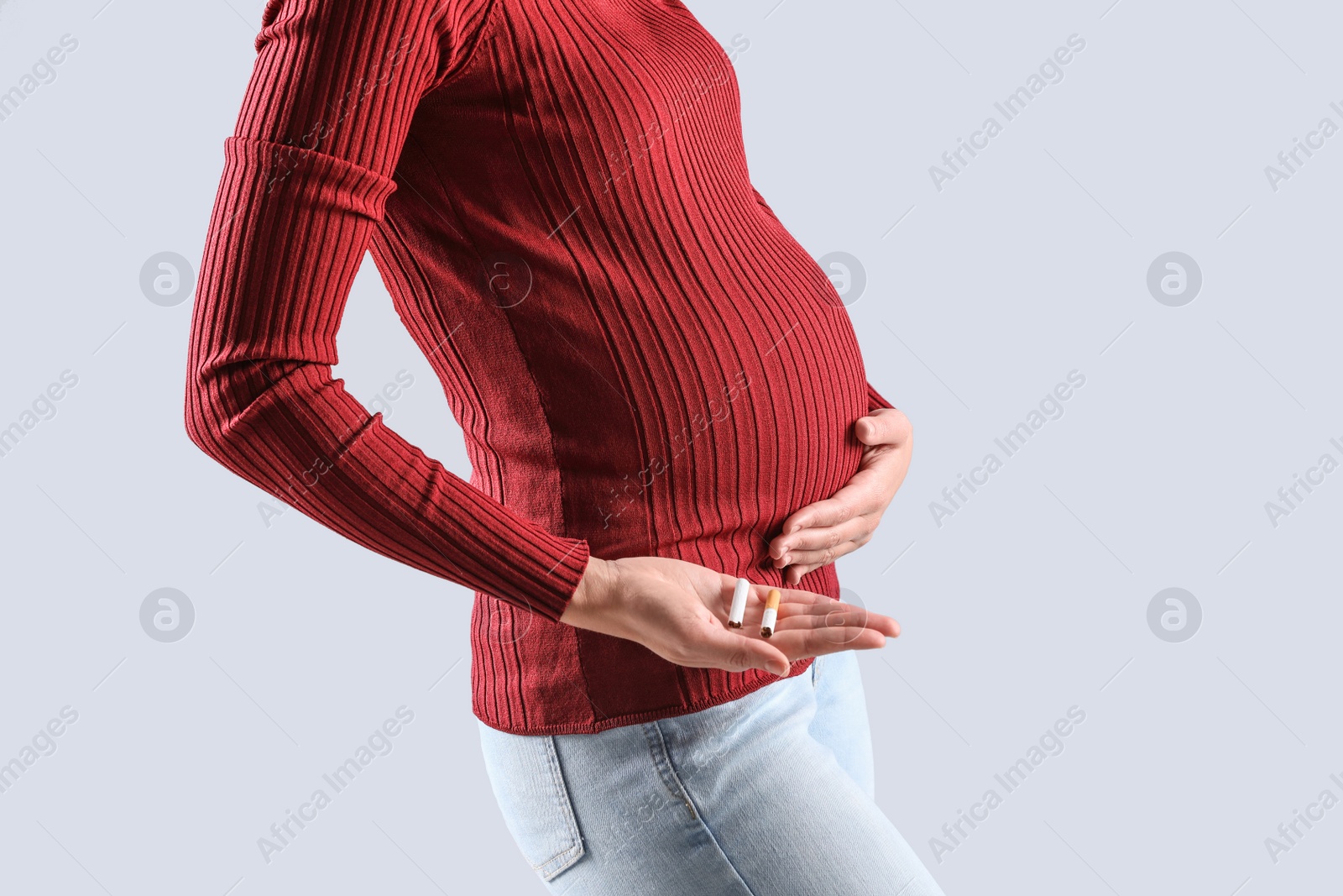 Photo of Young pregnant woman holding broken cigarette on grey background, closeup. Space for text