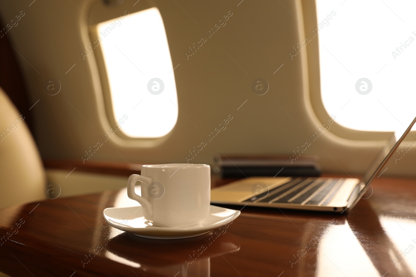 Photo of Cup of coffee with laptop and notebooks on table in airplane