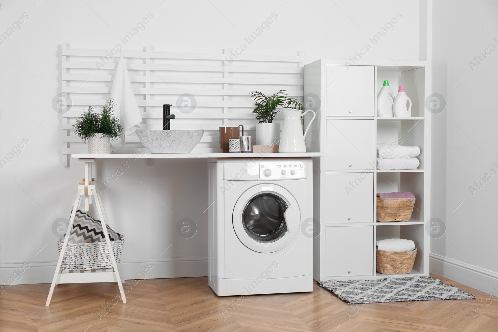 Photo of Laundry room interior with modern washing machine and shelving unit near white wall