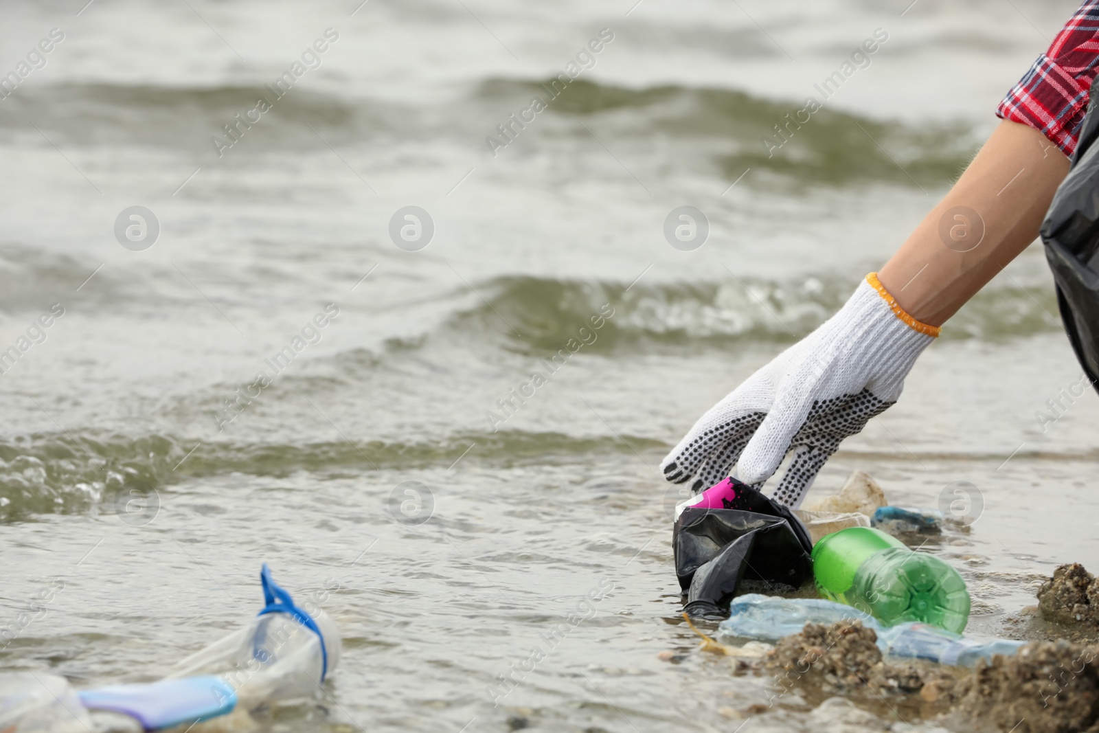 Photo of Woman in gloves collecting garbage on beach, closeup