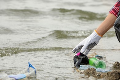 Photo of Woman in gloves collecting garbage on beach, closeup