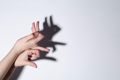 Shadow puppet. Woman making hand gesture like rabbit on light background, closeup. Space for text