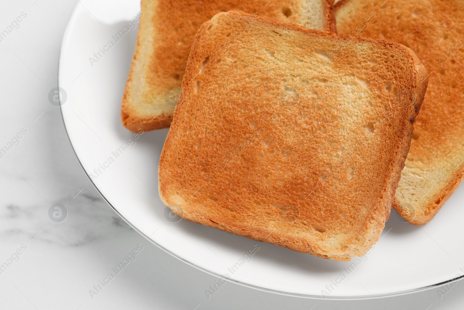 Photo of Slices of tasty toasted bread on white marble table, closeup
