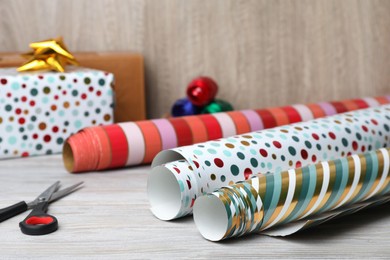 Photo of Different colorful wrapping paper rolls and scissors, on white wooden table, closeup